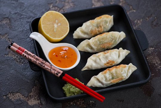 Cast-iron serving pan with fried korean dumplings, lemon, dipping sauce and chopping sticks. Horizontal shot on a brown stone background