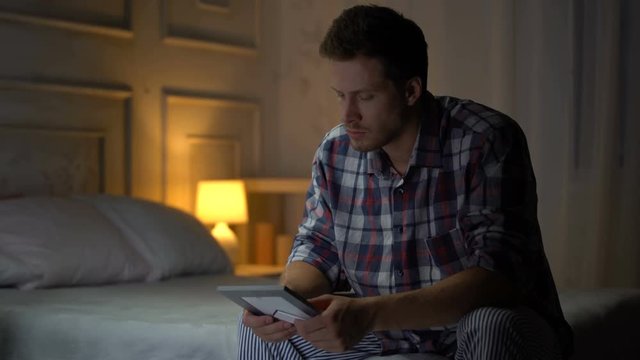 Unhappy lonely young male sitting on bed looking at photo, breakup, missing wife