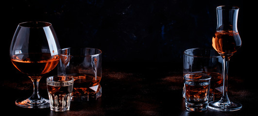 Selection of strong alcoholic drinks in glasses and shot glass in assortent: vodka, rum, cognac, tequila, brandy and whiskey. Dark vintage background, selective focus, copy space