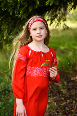 Cute blond young girl posing in a russian traditional red dress near fir tree