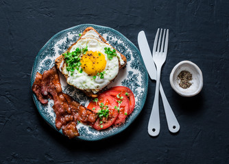 Nutritious breakfast - fried egg toast, bacon and tomatoes on a dark background, top view