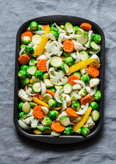 Raw ingredients for cooking vegetarian lunch - seasonal vegetables - brussels sprouts, carrots, cauliflower, pumpkin, onion, sweet pepper on a baking tray on a grey background, top view