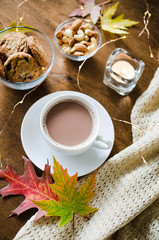 A cup of hot cocoa, nuts, cookies, candle and knitted plaid on a rustic wooden table.