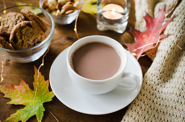 A cup of hot cocoa, nuts, cookies, candle and knitted plaid on a rustic wooden table.