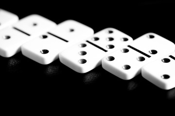 Dominoes are scattered on a dark surface close up. Black and white