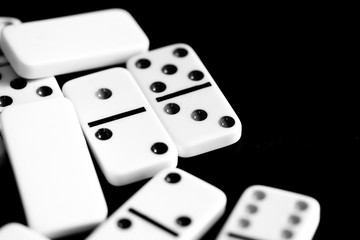 Dominoes are scattered on a dark surface close up. Black and white