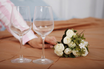 Two wine glasses and a bouquet of flowers on the bed with brown linens.