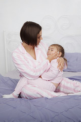 Young beautiful woman mother playing with her daughter with two pigtails in bed with blue bedclothes.