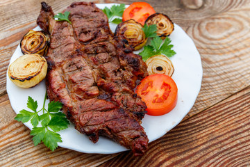 Grilled pork meat with onion, tomato and parsley in white plate on wooden table