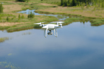 A flying white quadrocopter over a summer lake
