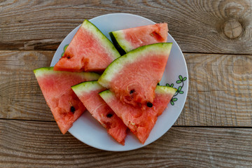 Fresh ripe sliced watermelon in white plate on rustic wooden table