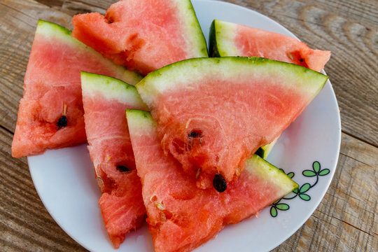 Fresh ripe sliced watermelon in white plate on rustic wooden table