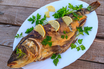 Baked carp fish with lemon and parsley on wooden table