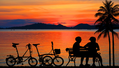 Fototapeta na wymiar Silhouette couple and bike relaxing on blurry sunset background.