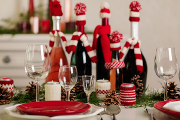 Merry Christmas and Happy New Year! Тable setting holiday knitted decor - Santa Claus knitted hats on the bottle with wine, candles in candlesticks in knitted decor.