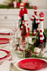 Merry Christmas and Happy New Year! Тable setting holiday knitted decor - Santa Claus knitted hats on the bottle with wine, candles in candlesticks in knitted decor.
