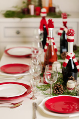 Merry Christmas and Happy New Year! Тable setting holiday knitted decor - Santa Claus knitted hats on the bottle with wine, candles in candlesticks in knitted decor.