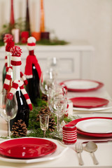 Merry Christmas and Happy New Year! Тable setting holiday knitted decor - Santa Claus knitted hats on the bottle with wine, candles in candlesticks in knitted decor.