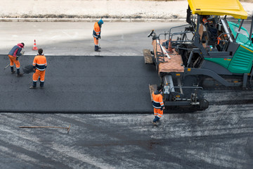 Asphalt paver machine and road construction workers on the road repair site. Road renewal process, construction working. High angle view