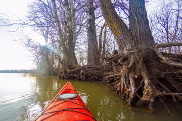 View from the red kayak on the river banks with autumnal trees in fall (winter) season. Danube river, autumn kayaking. Selective focus at kayak's prow.