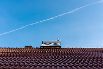 Frozen solar water heater boiler on rooftop, passing aeroplane, blue sky background.