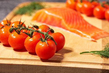 A piece of salmon on a wooden Board, tomatoes and dill. Selective focus