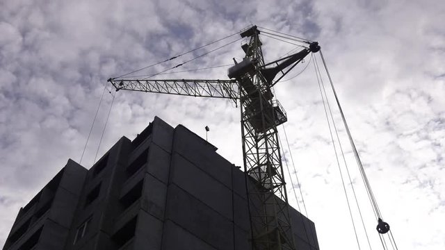Construction of a panel house. The facade of a prefab house without finishing. Construction crane lifts the panel. Hoisting construction works with tower crane during erection multistory building