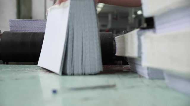 Male hands stack book blocks coming from the conveyor belt on a professional printing house.