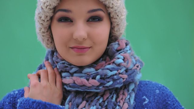 Happy calm girl in winter clothes looking at camera during winter holidays outside. Beautiful model in cap, coat, scarf standing against green screen copy space background. Happy winter woman outdoors