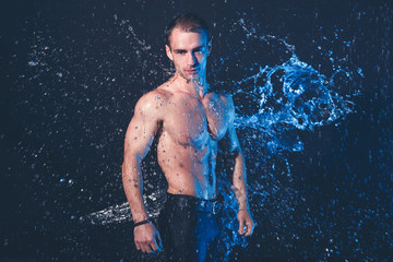 Fresh portrait of muscular man with water splashes on dark background.