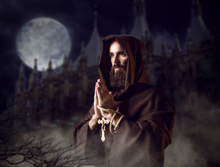 Medieval monk praying against castle and full moon