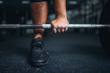 Powerlifter prepares for deadlift a barbell in gym