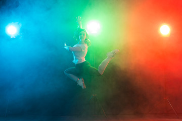 Fototapeta na wymiar Dancing, sport, jazz funk and people concept - young woman jump in the darkness under colourful light