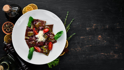 Ravioli with spinach, mushrooms and red wine sauce. In a plate on a wooden background. Top view. Free copy space.