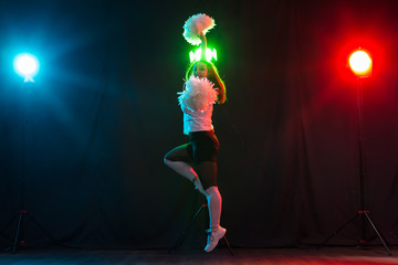 Dancing, sport, beautiful and people concept - young cheerleader girl in darkness show pom poms and...