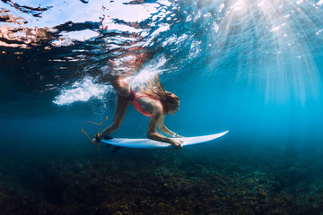 Surfer girl in bikini with surfboard dive underwater with under barrel ocean wave
