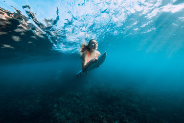 Fototapeta na wymiar Attractive surfer woman in bikini with surfboard dive underwater with under barrel wave