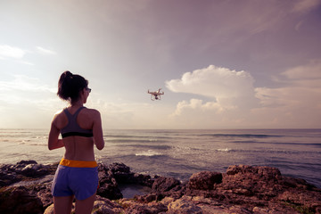 Woman photographer controlling a flying drone on seaside rock