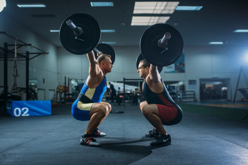 Two male weightlifters doing squats with barbells