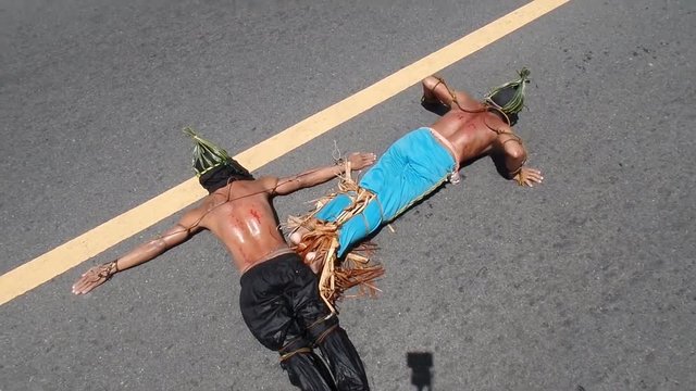 Unidentifiable maskedk penitent prone and lie prostrate on asphalt pavement beaten with bamboo stick imitating Christ&rsquo;s sufferings before crucifixion during Lenten week