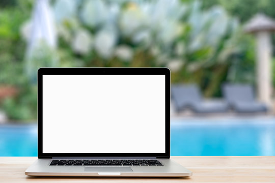 blank screen laptop on wooden table and swimming pool background