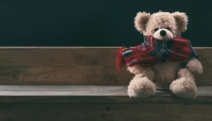 Fotobehang Cute teddy bear with scarf sitting alone on a wooden bench © Rawf8