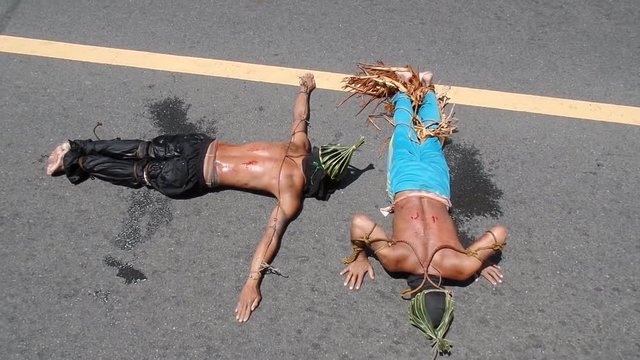 Unidentifiable maskedk penitent prone and lie prostrate on asphalt pavement beaten with bamboo stick imitating Christ&rsquo;s sufferings before crucifixion during Lenten week