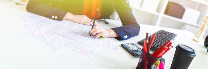 Beautiful young girl is working with documents in the office at the table and is holding a pencil...