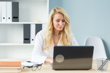 Working, business, technology and people concept - young blonde woman watching something in screen of laptop and smiling