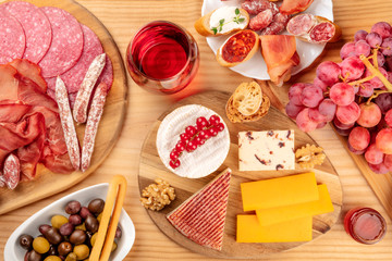 Charcuterie Tasting. A photo of many different sausages and hams, deli meats, and a cheese platter, shot from the top on a rustic background with a glass of red wine, olives and grapes