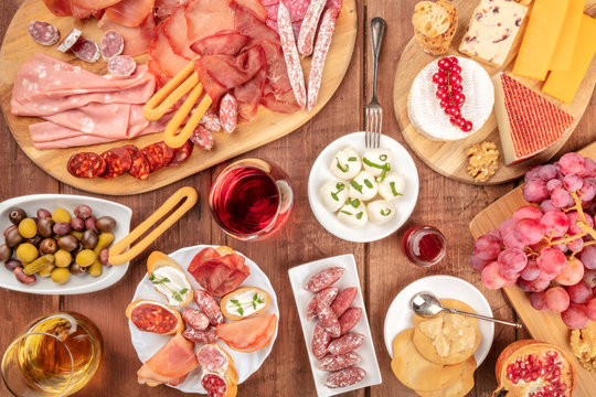Charcuterie Tasting. Many different sausages and hams, deli meats, and a cheese platter, shot from the top on a rustic background with glasses of wine, olives and grapes