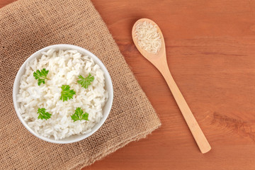 A photo of a bowl of cooked white long rice, shot from the top on rustic textures with a wooden spoon with dry rice and copy space