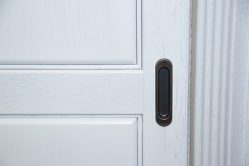 Dark handle on the white facade of the cabinet. Furniture fittings.
