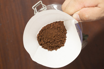 Hand hold a cup of drip coffee with paper filter tool on wood background